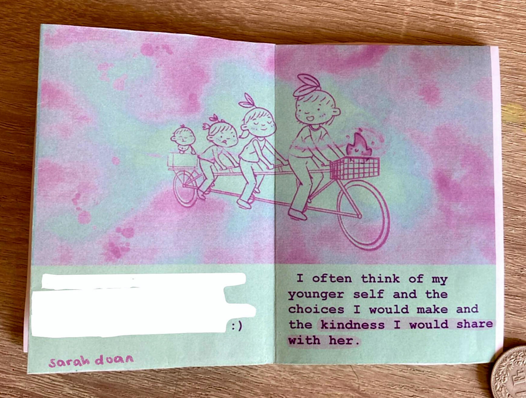 Photograph of zine with four people on a tandem bike as a baby, kid, teen, adult. Text reads "I often think of my younger self and the choices I would make and the kindness I would share with her."